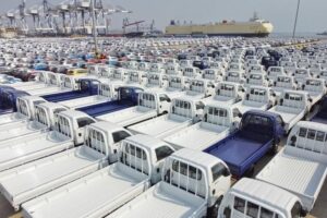 Reihenweise Pick-up-Transporter auf einem Hafenplatz vor einem Autotransportschiff