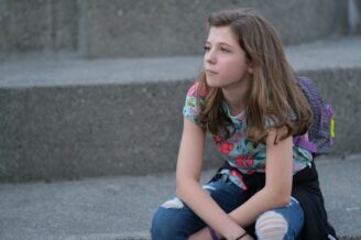 Nachdenkliches Mädchen mit Rucksack sitzt auf einer grauen Steintreppe